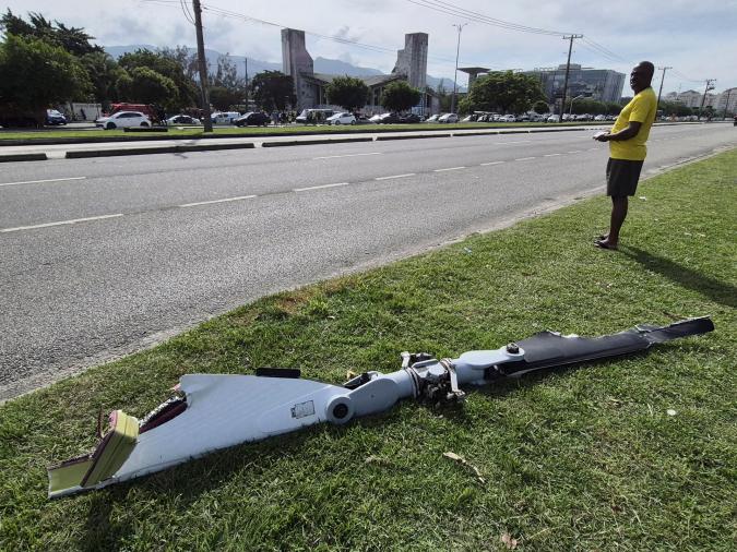 A man stands along a grassy area near a road, observing a large aircraft part lying on the ground.