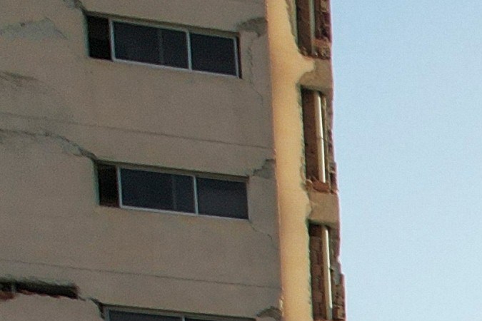 View of damaged residential buildings following a disaster, with debris scattered around and an empty street in the foreground.