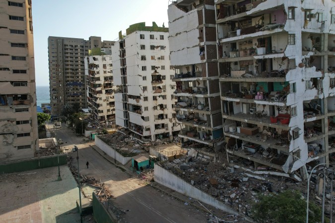 View of damaged residential buildings following a disaster, with debris scattered around and an empty street in the foreground.