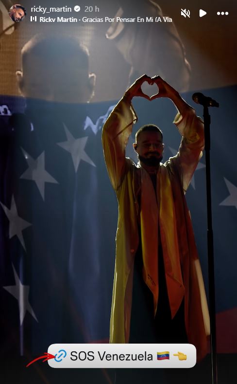 Ricky Martin performing on stage, making a heart shape with his hands against a backdrop featuring the Venezuelan flag.