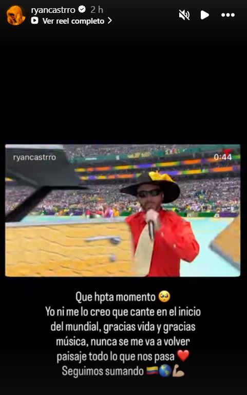 A performer on stage singing at a sporting event, dressed in a colorful outfit and hat, with a large crowd in the background.